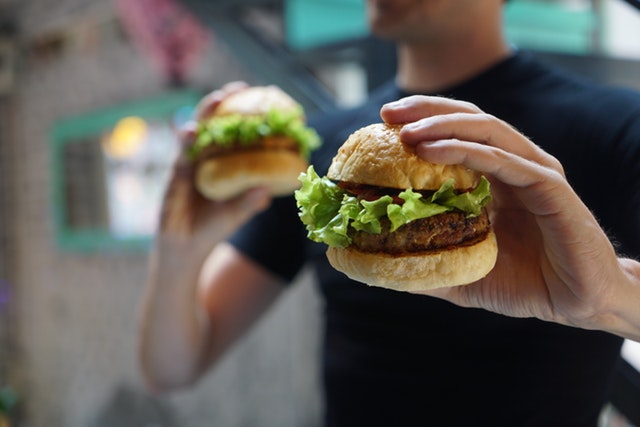 Muž drží v ruke dva hamburgery.jpg