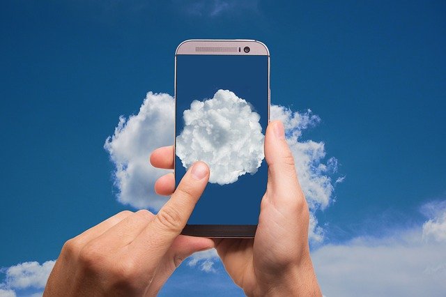 Človek ťuká na smartphone, ktorý má na obrazovke oblohu s mrakmi